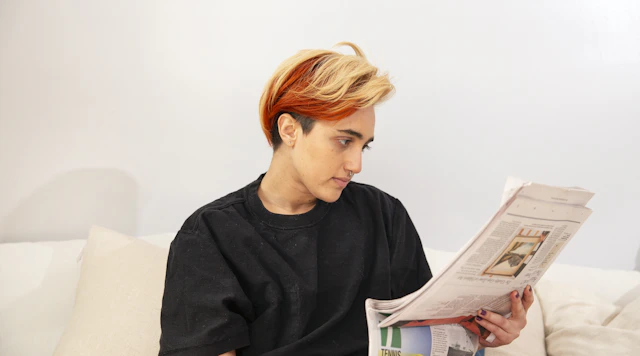 A transmasculine gender nonconforming person reading the newspaper