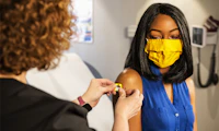 A woman of color receives a bandaid after a vaccine.