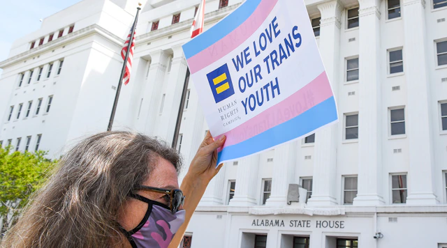 Person holding HRC "We Love Our Trans Youth" sign in front of Arkansas State House