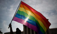 A large rainbow flag is waved in front of the US Supreme Court.