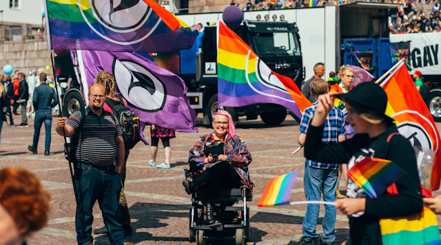Image of people at a Pride event holding rainbow Pride flags with the person in the center in a wheelchair.