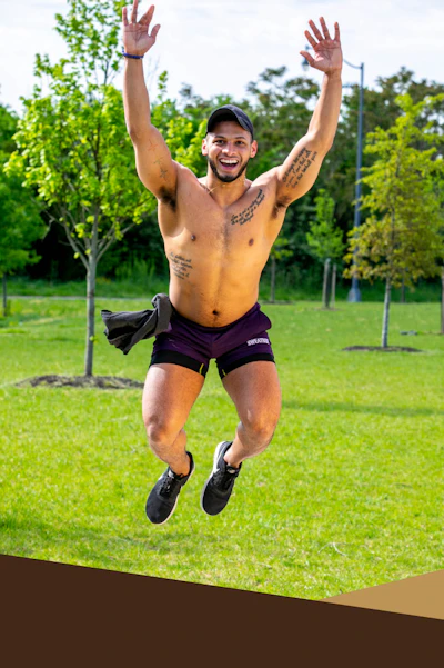 Black man not wearing a shirt jumping in the air while working out.