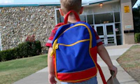 A young child wearing a blue backpack walks into a school building.