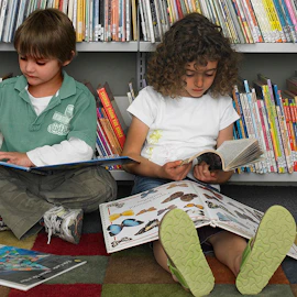 Two young children reading books on a library floor.